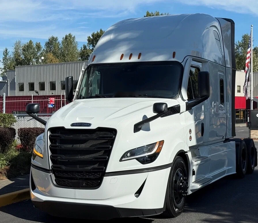 White Freightliner Cascadia sleeper tractor with the American flag behind it